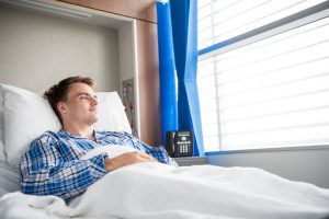 Male patient wearing pyjamas lying in bed with head propped up against pillow. Recovering in hospital.